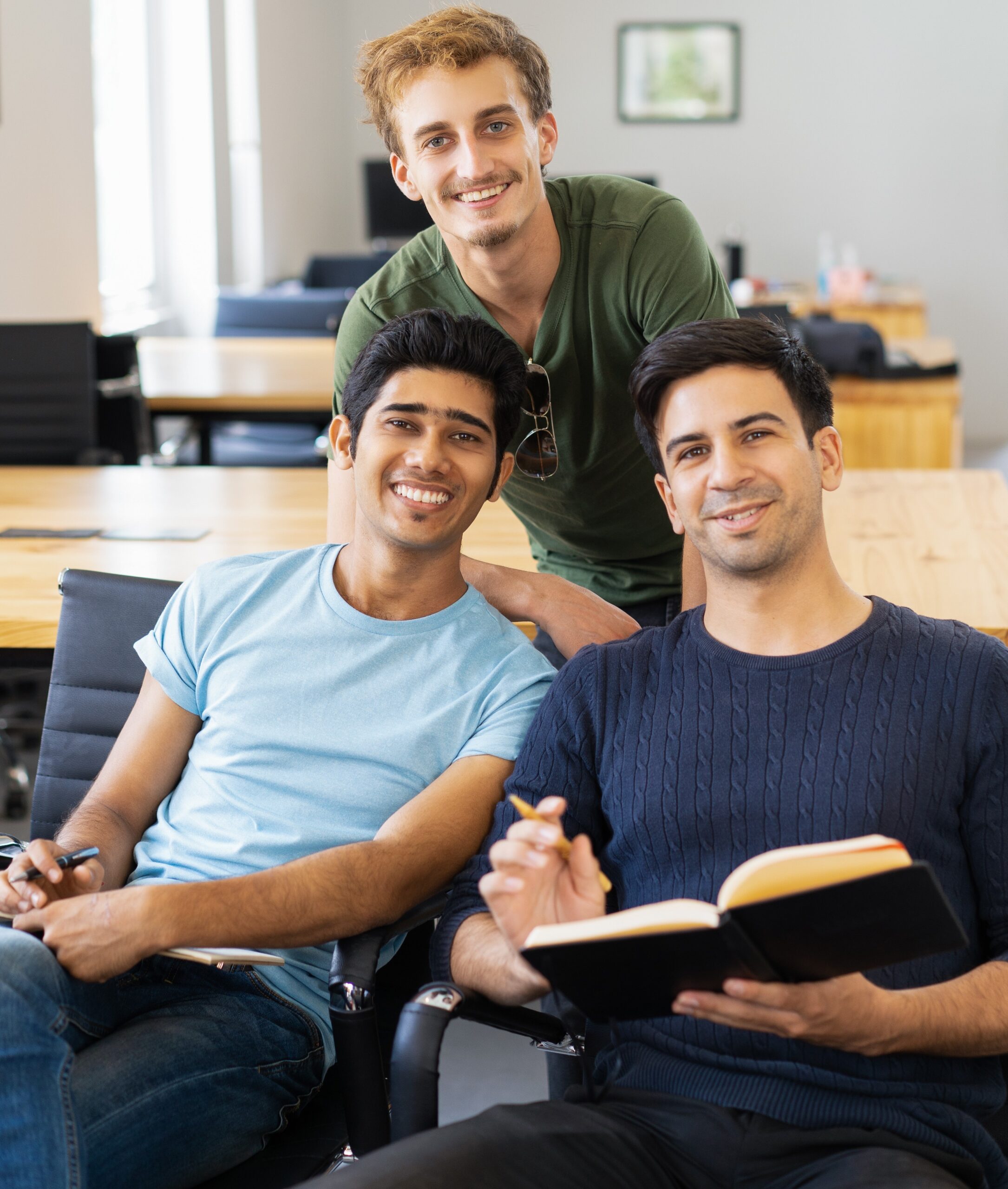 Three happy fellow students studying and looking at camera